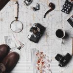 Budget Travel Experience - camera, pair of brown shoes, white ceramic mug, grey and black pen, brown smoking pipe