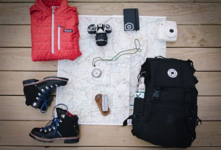 Outdoor Gear - black hiking backpack near white Fujifilm instax mini camera near black leather boots, red half-zip jacket, gray pocket watch on white map