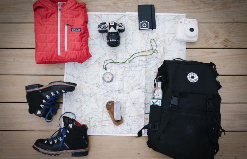 Outdoor Gear - black hiking backpack near white Fujifilm instax mini camera near black leather boots, red half-zip jacket, gray pocket watch on white map