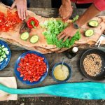 Cooking Classes - person slicing green vegetable in front of round ceramic plates with assorted sliced vegetables during daytime