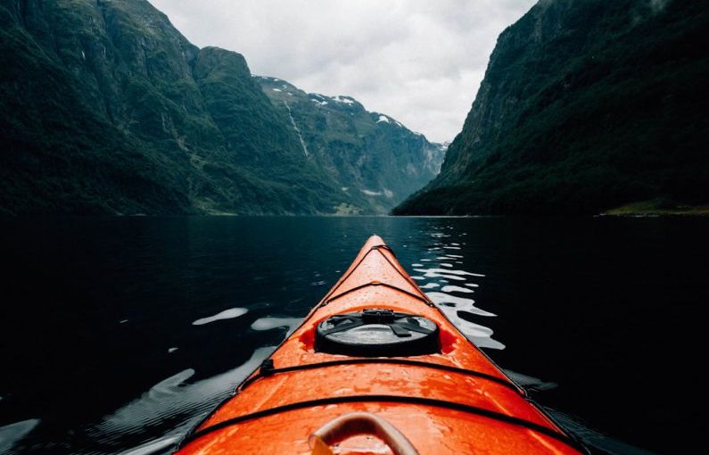 Kayaking Fjords - orange canoe on lake surrounding with mountain at daytime