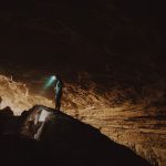 Cave Spelunking - person in blue jacket standing on brown rock formation during daytime