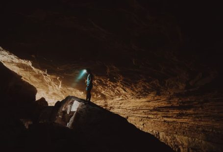 Cave Spelunking - person in blue jacket standing on brown rock formation during daytime