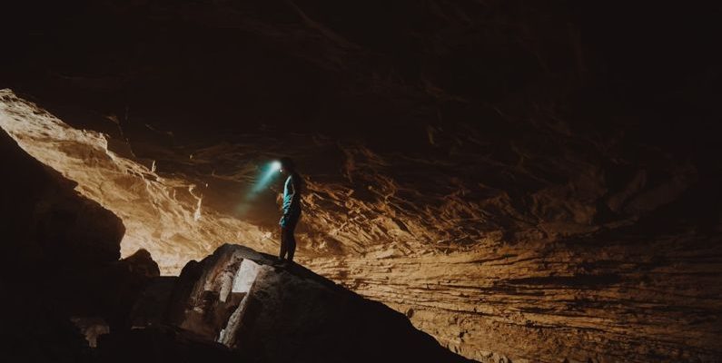 Cave Spelunking - person in blue jacket standing on brown rock formation during daytime