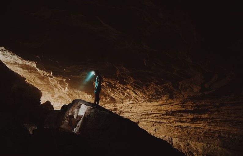 Cave Spelunking - person in blue jacket standing on brown rock formation during daytime