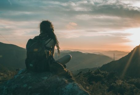 Solo Traveler Sunset - woman sitting on rock carrying black backpack