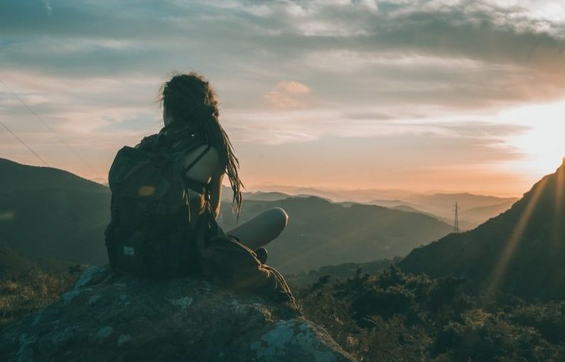 Solo Traveler Sunset - woman sitting on rock carrying black backpack