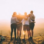 Volunteering Travel - four person hands wrap around shoulders while looking at sunset