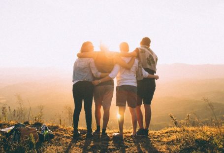 Volunteering Travel - four person hands wrap around shoulders while looking at sunset