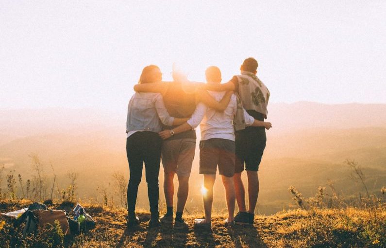 Volunteering Travel - four person hands wrap around shoulders while looking at sunset